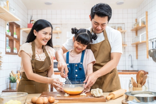 Seorang anak perempuan sedang memasak bersama Ibu dan Ayahnya