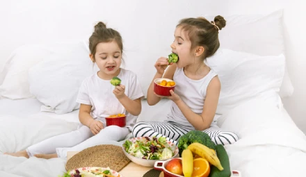 Dua anak perempuan sedang makan buah dan sayur yang tinggi serat pangan.