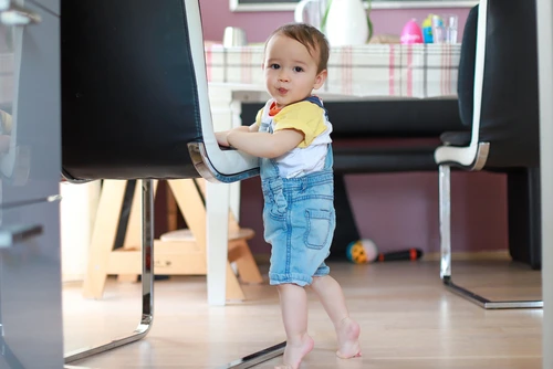 Bayi sedang berdiri sambil berpegangan kursi.