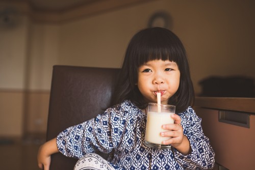 Anak perempuan sedang minum susu di gelas